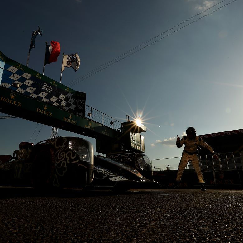 Rolex and Endurance Racing Person in one-piece racing suit with a helmet gives thumbs up to a racecar